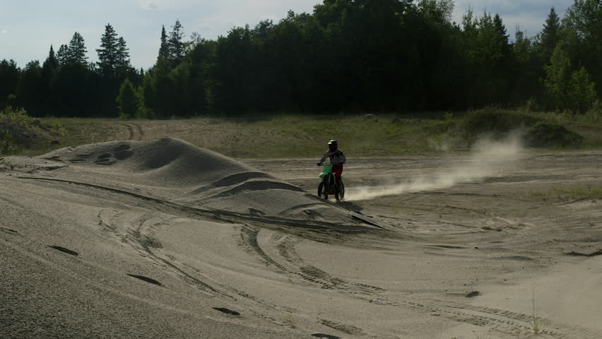 Dirt biker jumps sand pile in abandoned quarry - catches big air - on summer day - slow motion