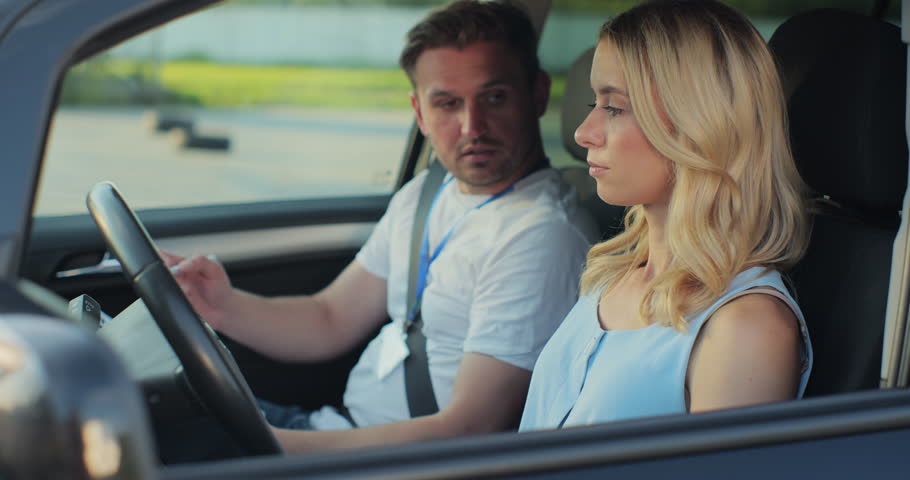 Young woman and driving school instructor with clipboard talking in car. Woman listening to instructor in car learning to drive. Royalty-Free Stock Footage #1107806985
