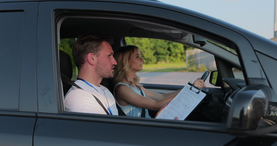 View of driving instructor holding checklist while in background female student steering and driving car. Driver courses, exam and people concept. Royalty-Free Stock Footage #1107807011