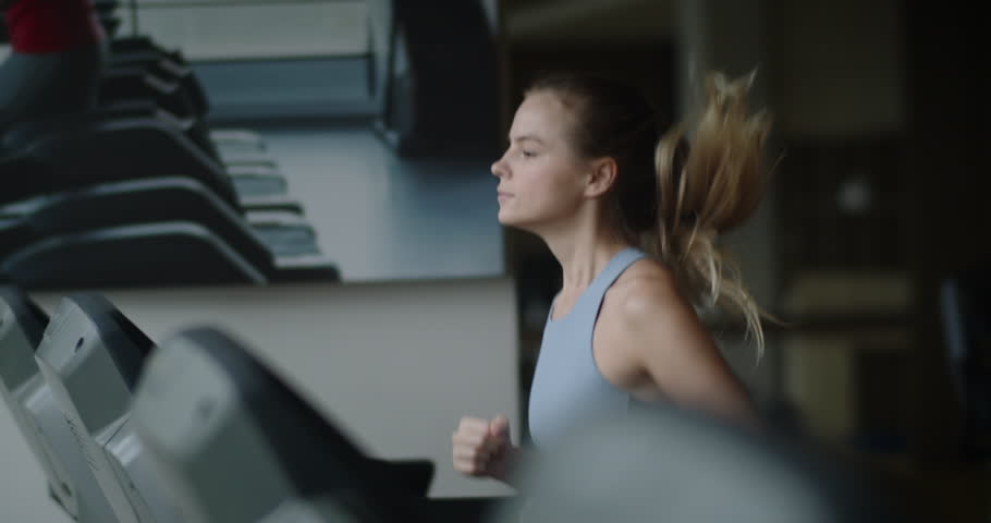 Fitness woman running on a treadmill in the gym. Athlete uses a running machine in a fitness center. Pretty girl doing cardio training in a sports club. 4K Slow motion Royalty-Free Stock Footage #1107807781