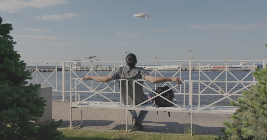 A young tourist man walks along a beautiful embankment among the trees.