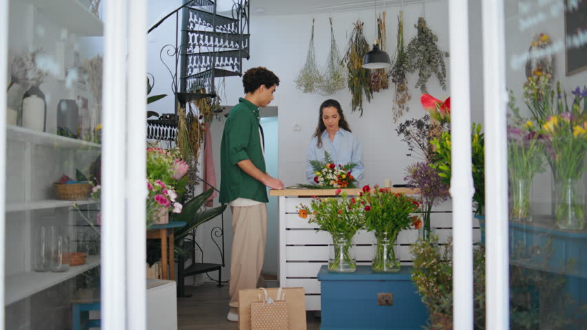 Smiling florist sell flowers to african buyer in floristry store. Relaxed brown skin client get shop anniversary gift celebration. Professional woman worker enjoy flower composition. Business concept.