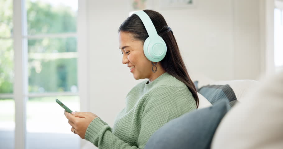 Woman, sofa and headphones with phone for music streaming service, social media and network at home. Person or online user scroll internet or website with audio, electronics and mobile subscription Royalty-Free Stock Footage #1107822207