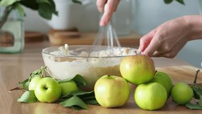 Knead the dough for the apple pie. A bowl of dough. Autumn mood to cook apple pie-charlotte. Women's hands hold a whisk in their hands and mix the batter. Video lesson, video recipe-step-by-step