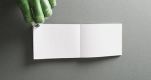 Vertical video of halloween green monster hands and notebook with copy space on grey background. Halloween, tradition and celebration concept.