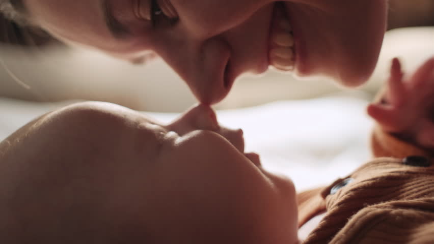 Selective focus of smiling loving mother and baby touching noses, enjoying tender moment, lying on cozy bed at home, happy young mom with newborn child kid having fun, motherhood and childcare concept