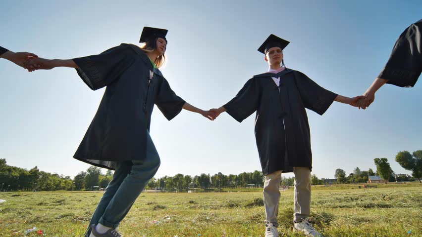 College graduates holding hands run in a round dance. | Shutterstock HD Video #1107834557