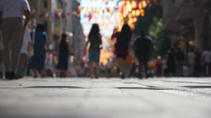 Low-angle close up of blurred people crowd feet walking by paving slabs on pedestrian street . Popular Istiklal Avenue leading to Taksim Square. Istanbul, Turkey