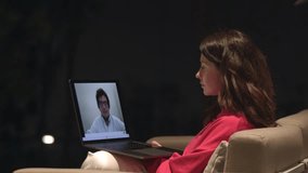 Woman having an online video conference, laptop screen with a man talking. Home interior with sofa, late conversation with a business partner. Concept of network and communication