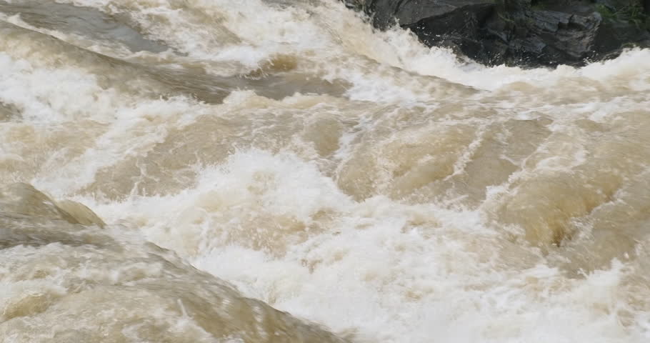 Strong fast stream of mountain river flowing, closeup. Raging stream of brown water flood. Natural wild current background. Rapid abounding flow in mountains nature. 4k slow motion video. River splash