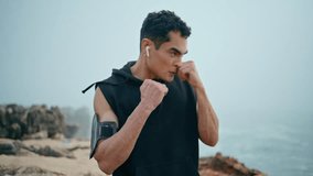 Strong boxer workout seaside closeup. Professional athlete punch air on cliff. Serious motivated sportsman training kickboxing in morning. Muscular guy practice looking camera. Outdoor cardio exercise