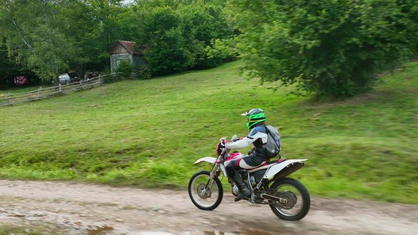 aerial shot of a motocross rider on a journey on a dirt and dusty country road driving fast and exploring beautiful nature while racing chased by the drone.