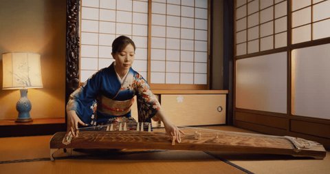Portrait of a Talented Female Playing Koto Plucked String Instrument in Traditional Japanese Home. Musician Wearing a Blue Kimono, Practicing to Play Historic Music Before a Concert วิดีโอสต็อก