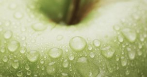 Micro video of close up of green apple with water drops and copy space. Micro photography, fruit, texture and colour concept.