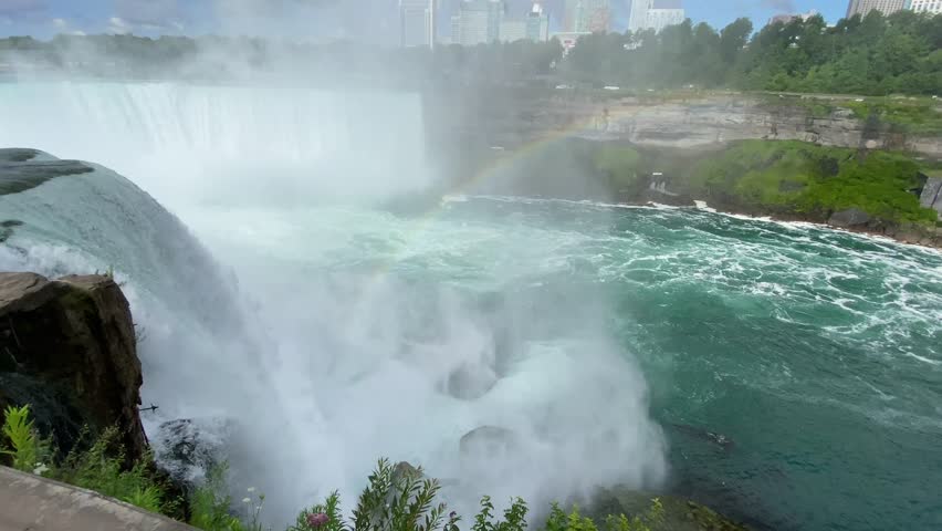 Close up looking at the edge of horseshoe falls with a rainbow in front.