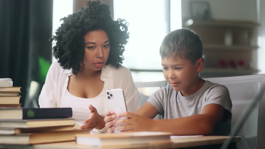 Bored primary school boy kid looking at smartphone ignoring mad mother screaming at him because studying at home Angry woman mom doing homework together indoors Children phone addiction concept Royalty-Free Stock Footage #1107850517
