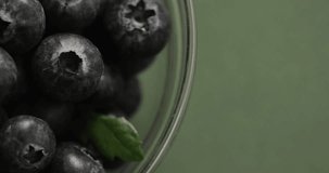 Micro vertical video close up of bowl of blueberries and copy space on green background. Micro photography, food, texture and colour concept.