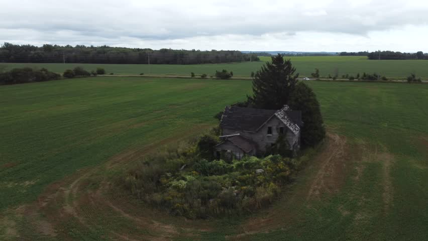 A drone panning around an old abandoned farmhouse on a cloudy day