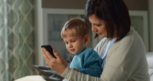 a young grandmother shows her grandson a video on his mobile phone and the child is surprised and happy when he sees it