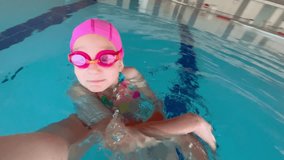 A child girl is playing in a bright sports swimsuit, flippers, a swimming cap and goggles for swimming under water A little girl in a swimming in the pool. Under water view.