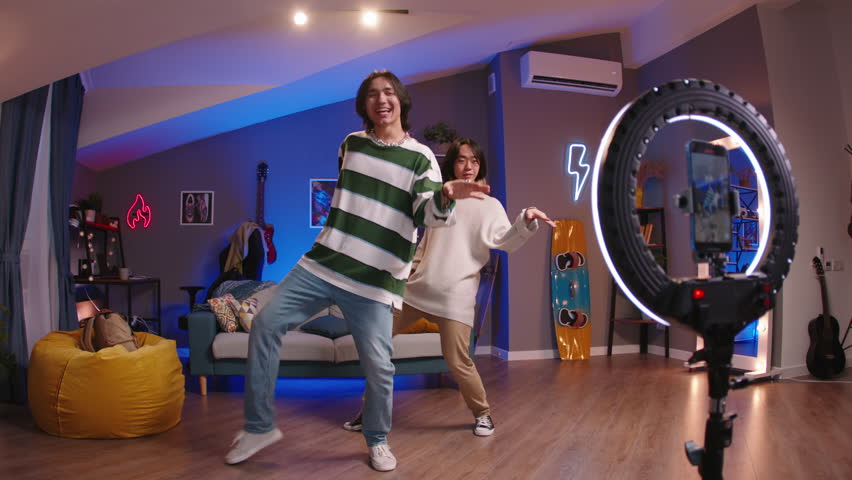 Two Asian Gen Z friends, K-pop dancers, are making trending videos for social media. Happy young independent content creators shooting K-pop dancing challenge tutorial flex, cringe mood for subscriber