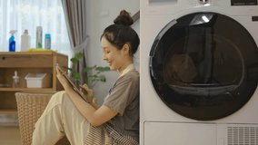 Young asian woman are playing with digital tablet in home sitting near the washing machine, while waiting for the washing machine to finish working - Powered by Shutterstock - Get 15% off with code: PIKWIZARD15