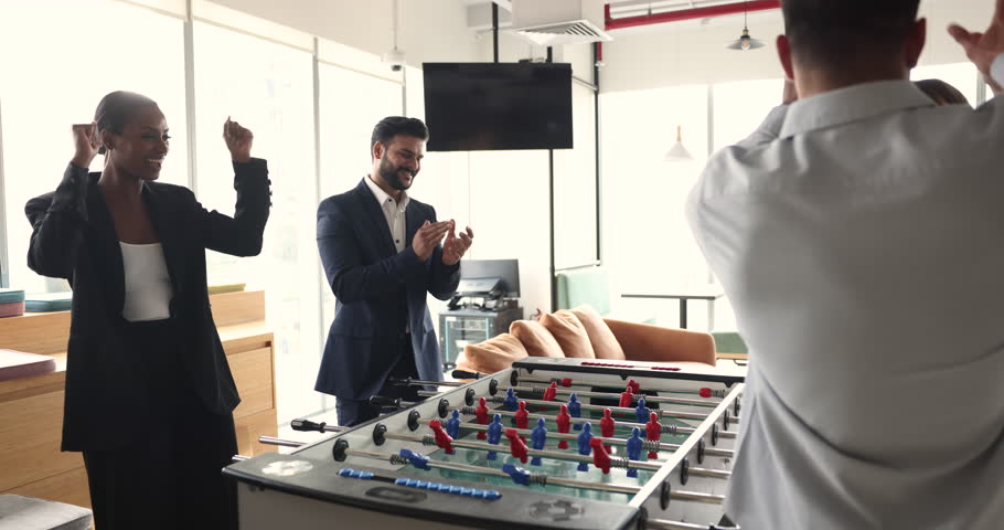 Happy workmates divided into two groups play table soccer, having fun during break in co-working. Boost team spirit, winning, express unity, give high five. Office friends enjoy tabletop football game Royalty-Free Stock Footage #1107875961
