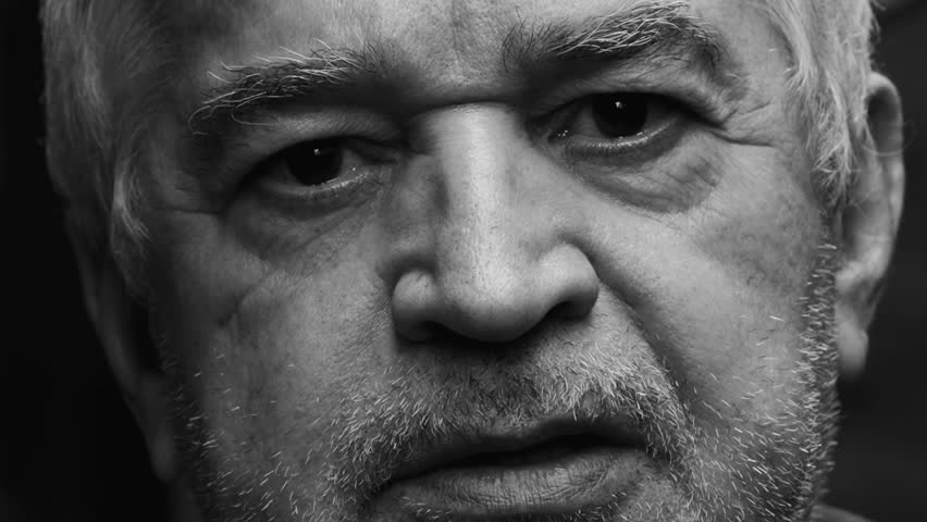 Dramatic portrait of a wrinkled senior man close-up face in monochromatic black and white photography staring at camera with stern concerned expression