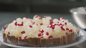 Close up of a chef's hand wearing black gloves laying an pomegranate seeds on top of a longan pie. Decorate the cake. The process of making an longan pie dessert at home in the kitchen. Bakery