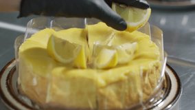 Close up Chef's hand in black glove is placing lemon slices circle on lemon curd cake. Decorate the cake. The process of making an lemon cake dessert at home in the kitchen. Bakery