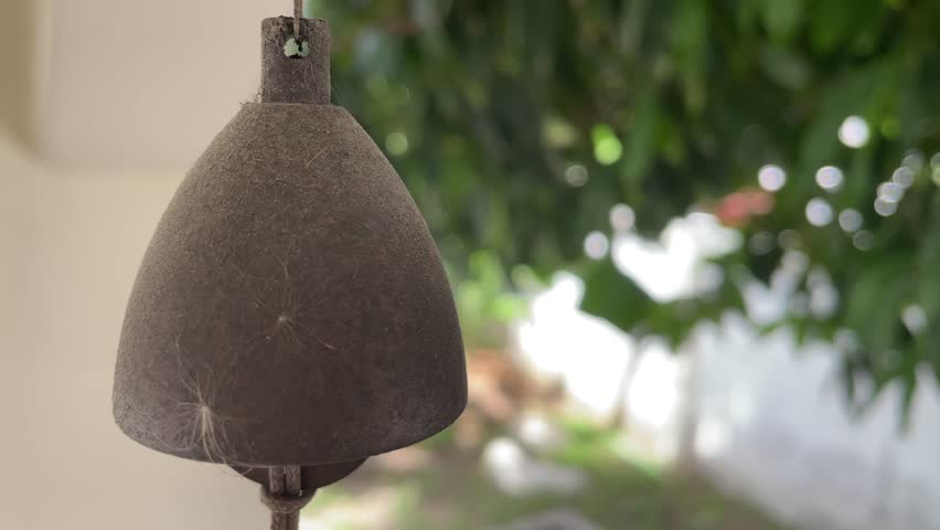 Vintage old rusty bell hanging from ceiling at home close up shot with blurred tree at home garden background sunny day