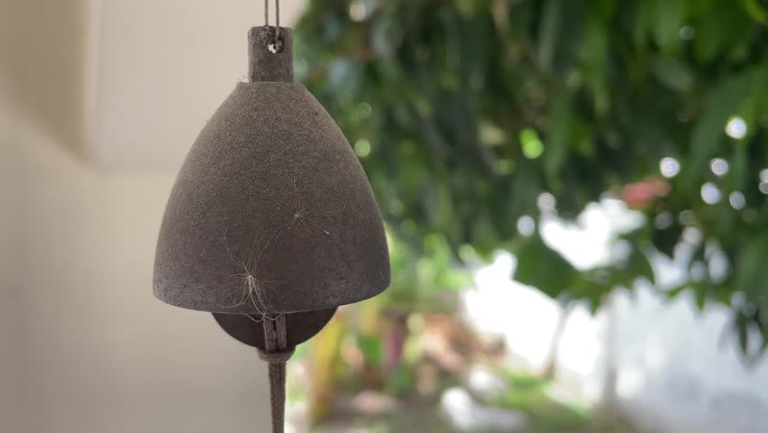 Vintage old rusty bell hanging from ceiling at home close up shot with blurred tree at home garden background sunny day