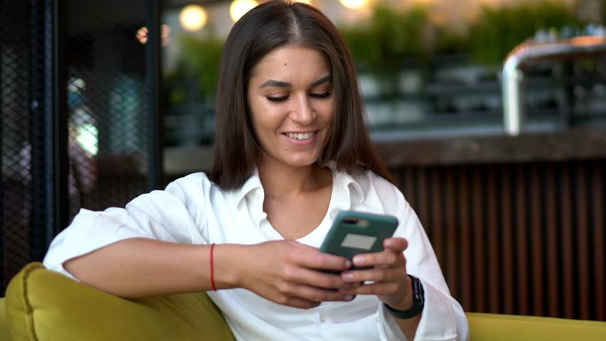 Cheerful hipster girl installing media application for browsing social networks during free time, happy Caucasian female blogger creating web publication via mobile technology
