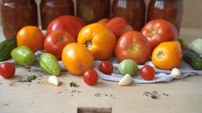 tomatoes are red and yellow, large and small spices cucumbers and garlic on a wooden table against the background of glass jars with canned vegetables. The concept of preparing blanks 
