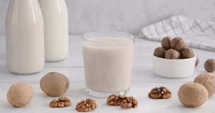 Vegan milk. Person taking a glass full of alternative milk made of walnuts, hand grabbing a glass from white wooden table, non-dairy product, 4k horizontal video, slow motion footage