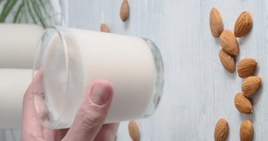 Person taking a glass with almond milk, Close-up video of vegan drink made of almond nuts placed on white table, 4k vertical video, slow motion footage 