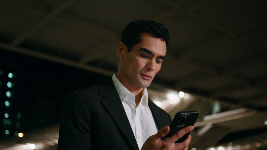 Happy man reading phone message crossing evening airport close up. Smiling business person looking smartphone screen walking alone at night lights town. Handsome manager holding cellphone at dark city