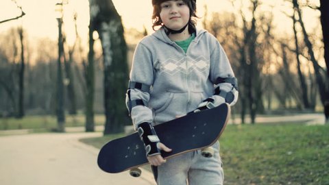 Young happy boy in helmet and protective pads with skateboard, outdoors
