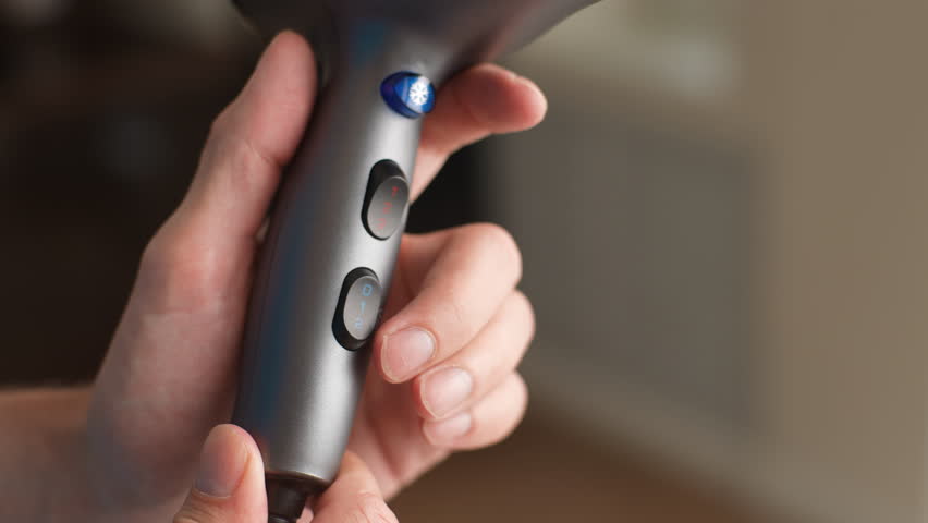 Close-up cropped shot of unrecognizable man pushes the buttons of state-of-the-art electric hand-held hair dryer, checking out different modes of operation. Shooting in slow motion.
