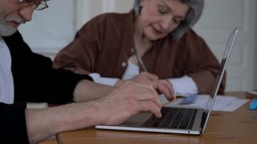 Caucasian mature couple collaborating on startup project during weekend time in home interior, skilled adult male and female graphic designers with laptop computer browsing web page 