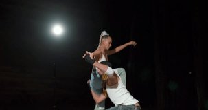 hip-hop dancers woman and man performing different tricks and movements while dancing in studio on black background, on stage, raising female on shoulders, flexible female, male give performance