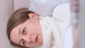 A European-looking woman with a cold is lying on a bed with a bandaged throat. Vertical video