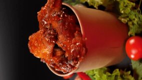 Vertical video. Spicy chicken wings doused in sauce swirl in a paper bucket.