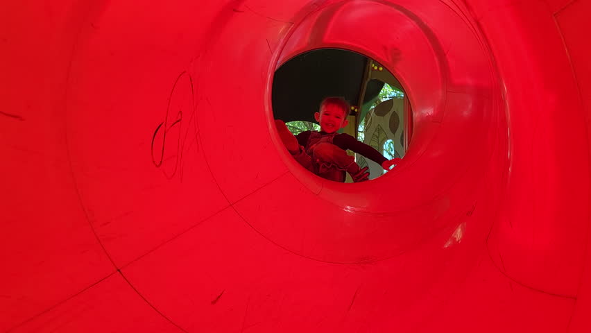 The baby is enjoying the slide on the playground with a cheerful smile. Kid boy aged two years (two-year-old)