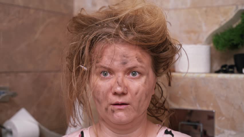 Blonde woman with unkempt hair sits in tiled toilet after small explosion. Female looks at one spot in bathroom with surprised and shocked expression | Shutterstock HD Video #1107920205