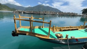 In the video, Fenniaolin Fishing Port in Yilan City, Taiwan is surrounded by mountains. The close-up shot shows a green fishing boat, turquoise sea water, blue sky and white clouds.