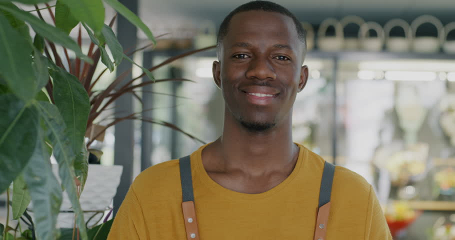 Portrait of flower store worker African American man standing indoors in shop smiling looking at camera. People and floristry business concept. Royalty-Free Stock Footage #1107928541