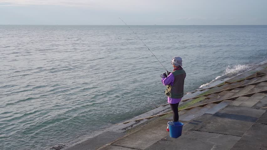 Tourist fishing alone by the sea. Photo from behind. see the wide sea, sunlight shines in