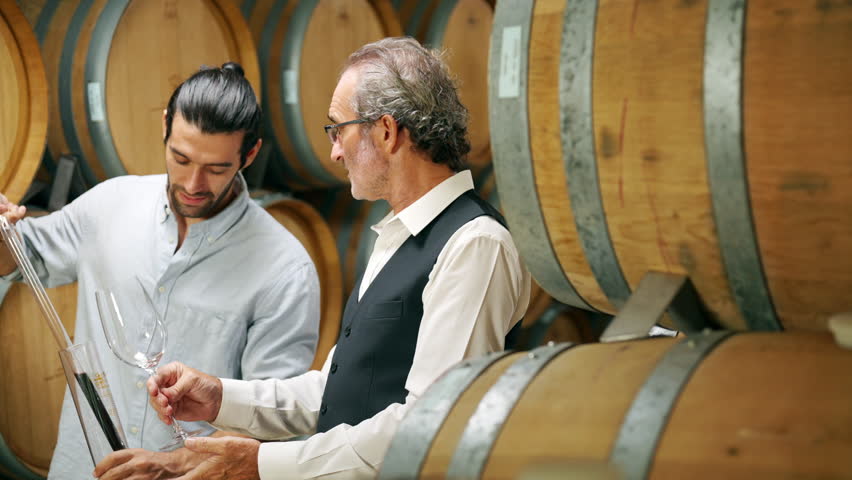 Professional senior man sommelier tasting red wine in wooden barrel at vintage wine cellar in wine factory. Winery, wine shop, brewery liquor manufacturing industry and winemaker business concept.