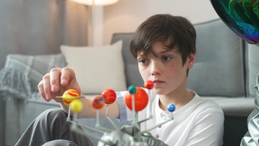 Little boy play in the living room at home, man in an astronaut costume sitting on the floor with her son, boy playing with a toy model of the solar system, study of astronomy.
